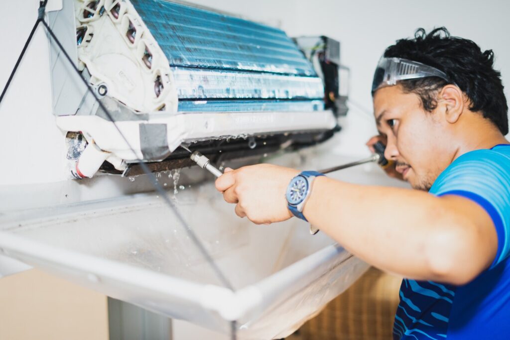 A technician repairs an air conditioner in a room, focusing on the unit while tools are nearby.