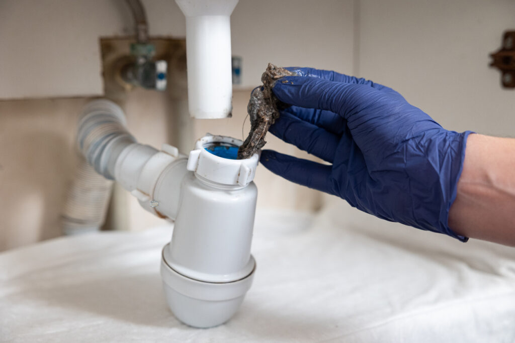 A man's hands clean the sink's siphon from dirt, pulling out clump of hair & dirt