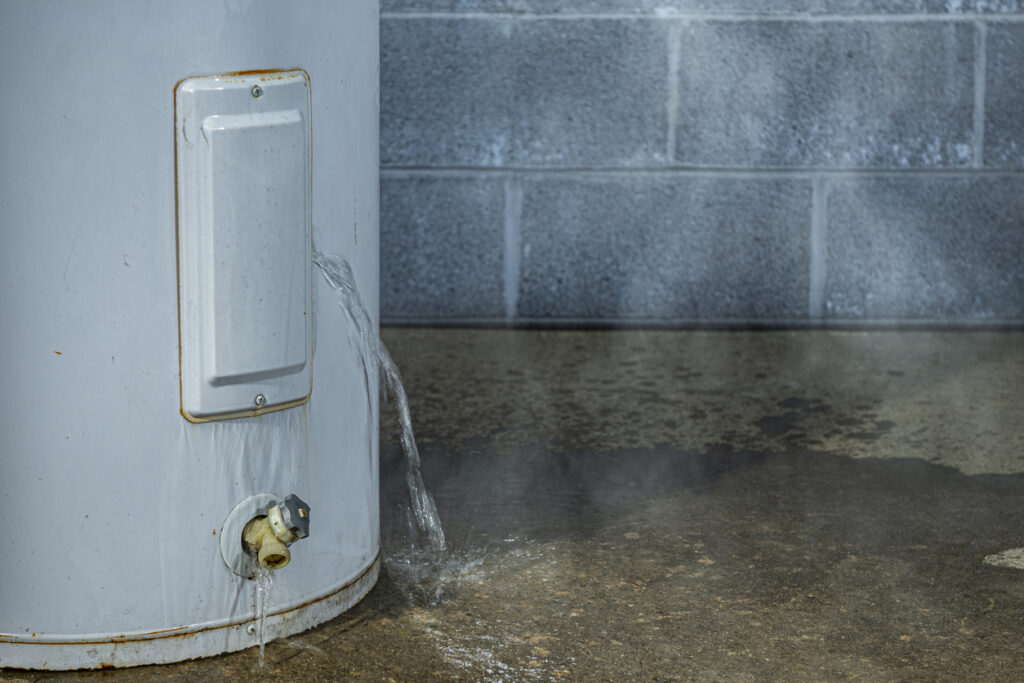 A close-up of a water heater leaking water on to the basement floor