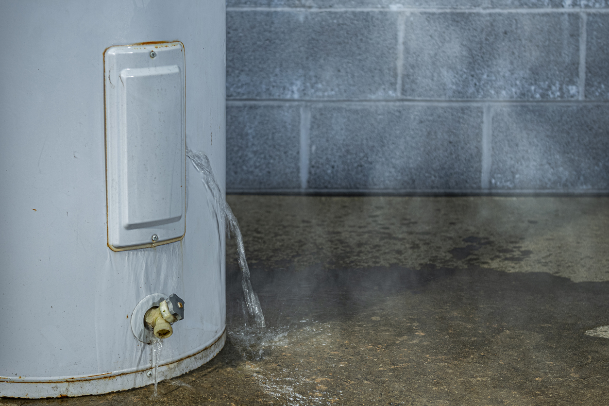 A close-up of a water heater leaking water on to the basement floor